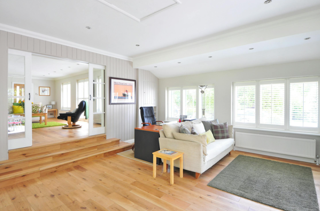 Living area with light wood floors, white walls, and large windows.