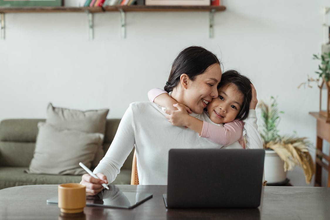 An image of a girl hugging her mother as she works