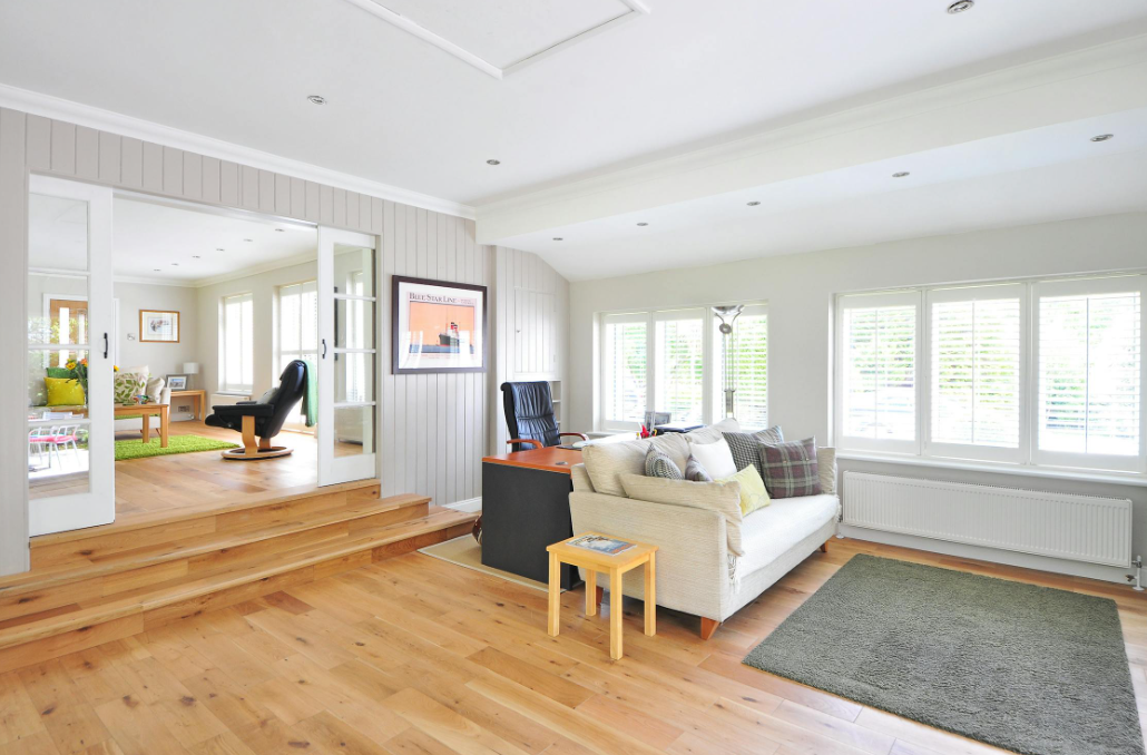 Living area with light wood floors, white walls, and large windows.