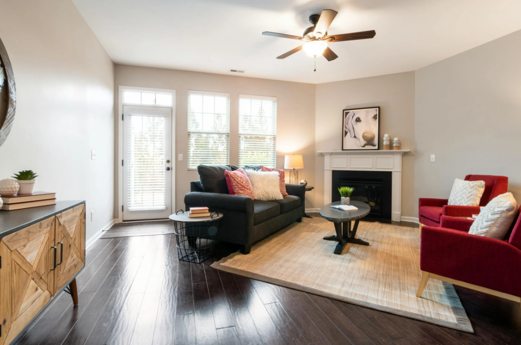 A room set up with a dark gray sofa, two red armchairs, a coffee table, and a TV stand.
