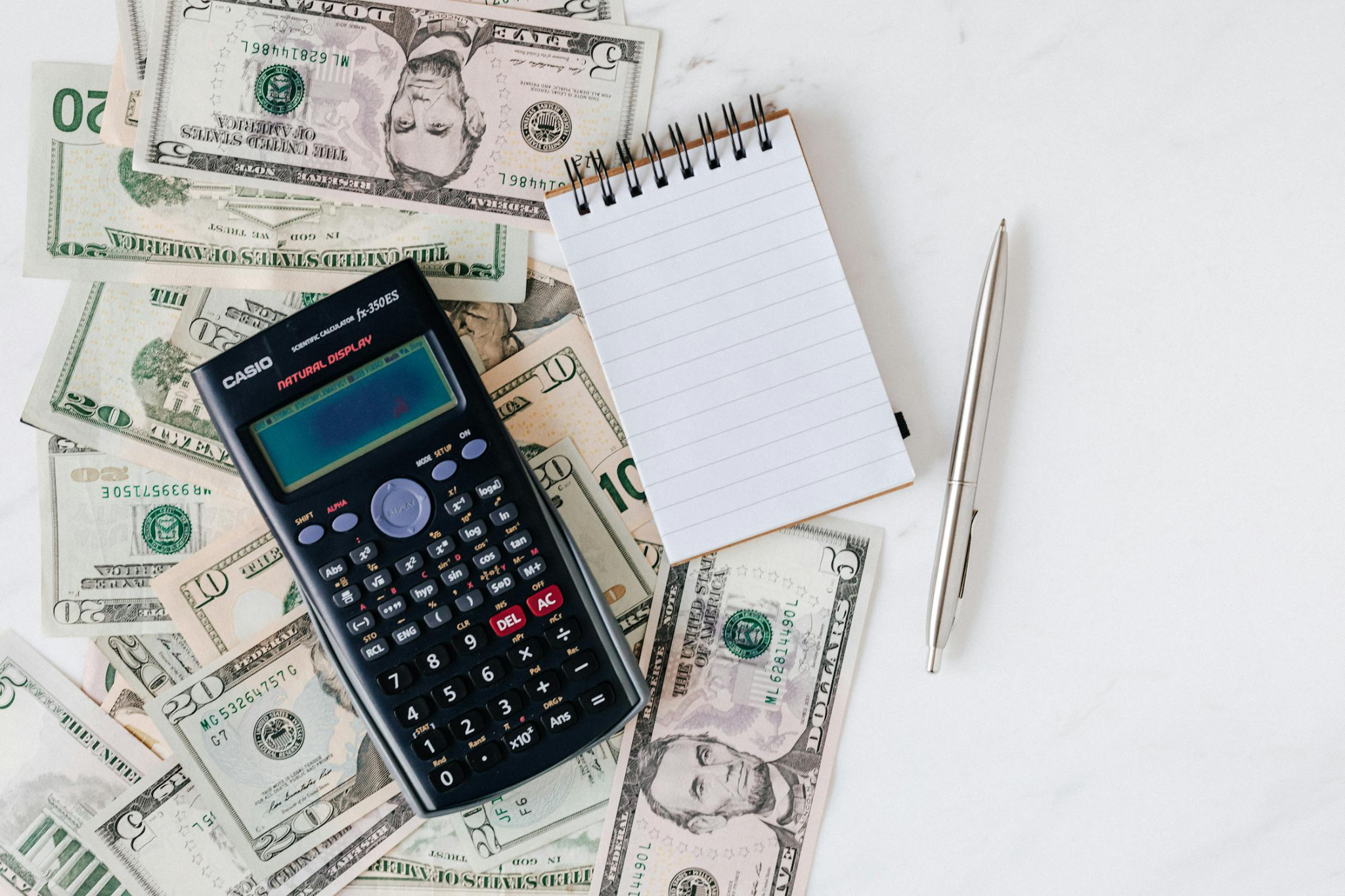 A scientific calculator, a notepad, a pen, and various U.S. dollar bills