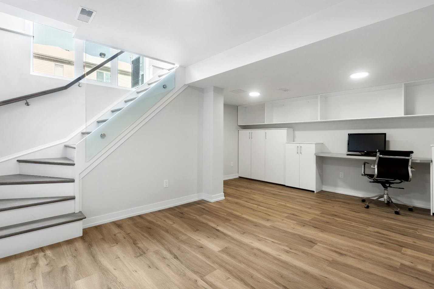 An image of a staircase leading down to a white basement with an office chair and a PC.