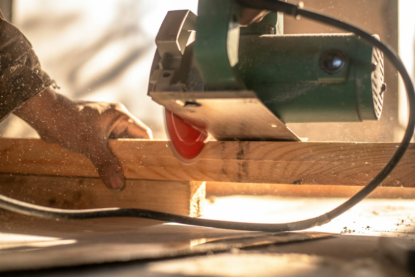A close-up of a circular saw cutting through a wooden plank during the early stages of a custom home build, with a worker’s hand guiding the wood.