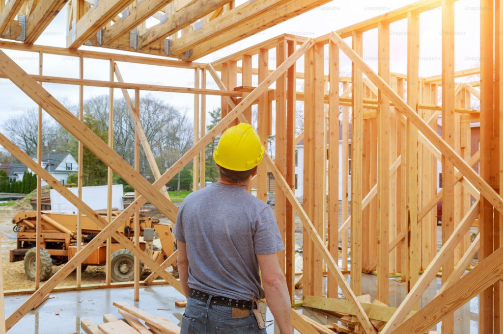 Back shot of a builder looking at the wooden structure of a house under construction.