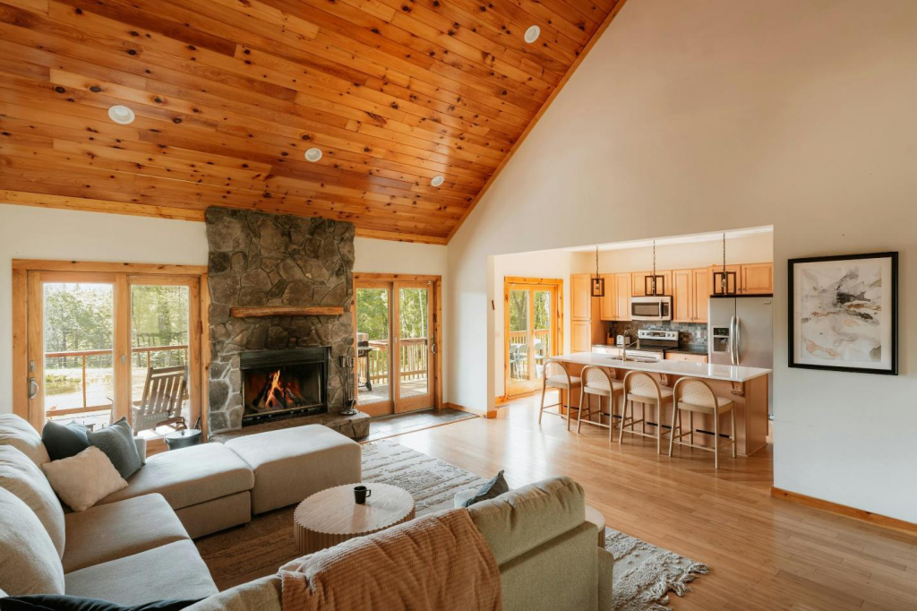 A cabin’s living room with open-space kitchen, sofas, coffee table, and fireplace.