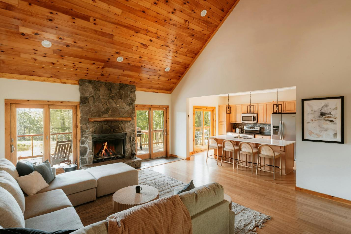 A cabin’s living room with open-space kitchen, sofas, coffee table, and fireplace.
