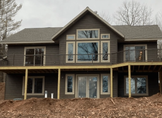 Completed multi-level custom home with large windows and an elevated deck overlooking a wooded property