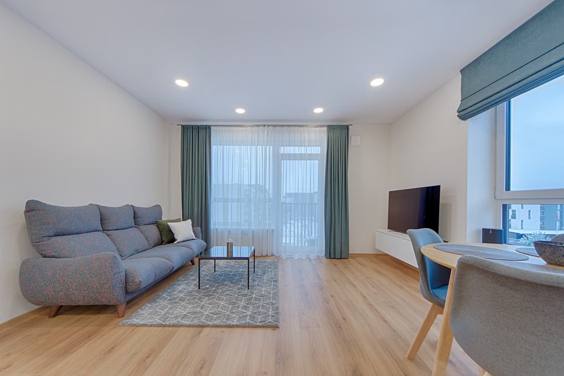 Bright living room with a grey sofa, a small coffee table, and large window curtains